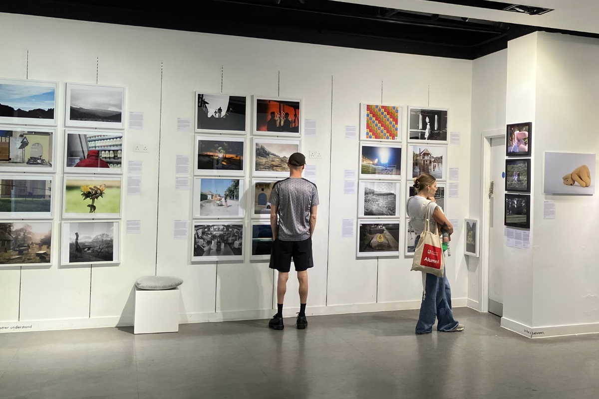 Two people examining framed photos on display on the walls in a gallery.