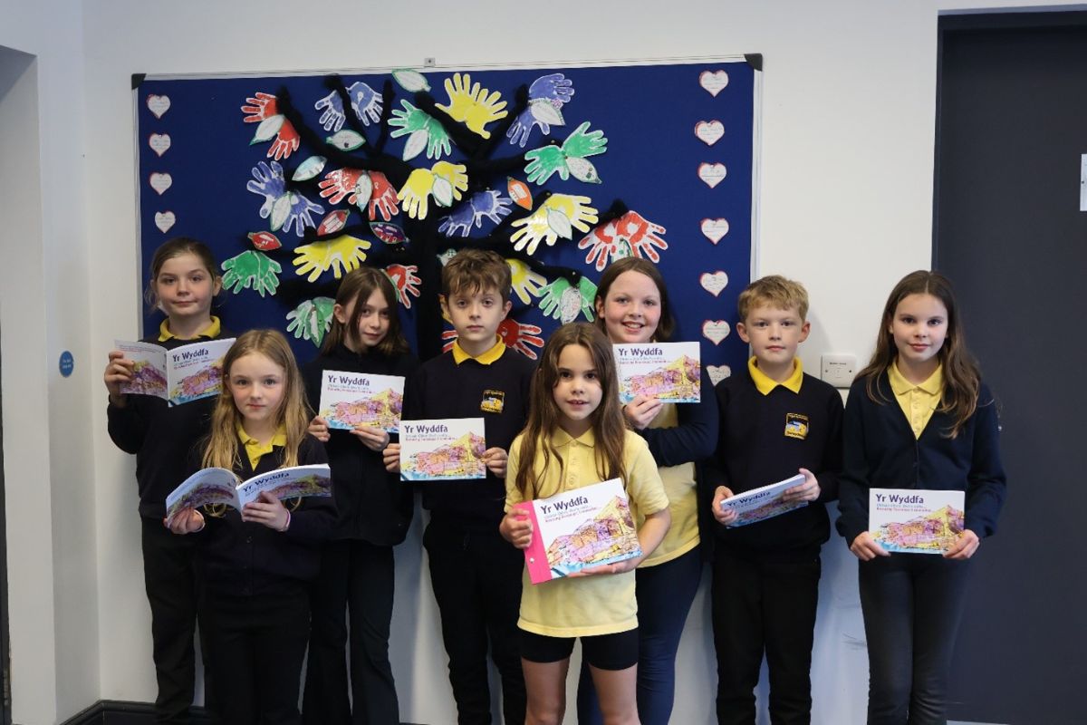 A group of eight school pupils - boys and girls - each holding a copy of the new poetry book. They are all standing in front of artwork of hearts, hands and leaves.