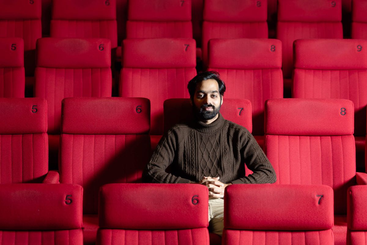 A man sat alone in a cinema seat, facing the camera.