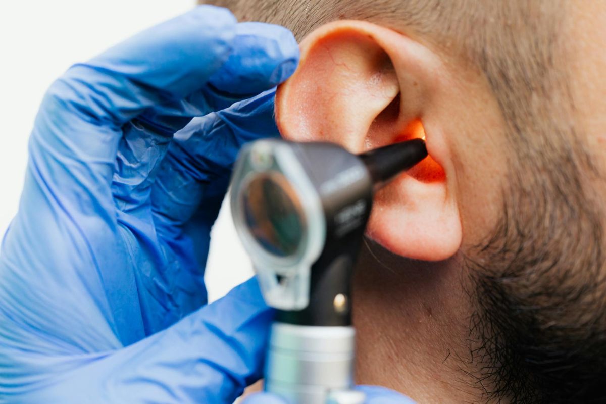 A close-up of an ear. An otoscope is being used to check inside the ear by someone wearing blue gloves.