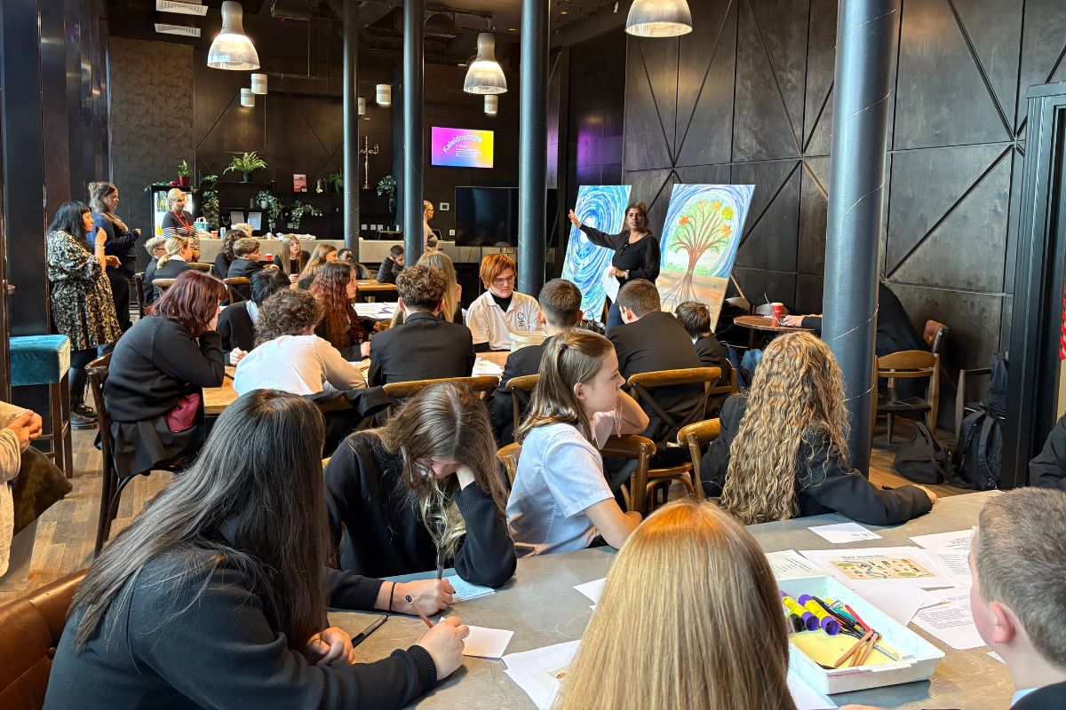 A packed room at Storyhouse with schoolchildren sat at tables. Artwork is in the background. A woman is giving a talk in the background.