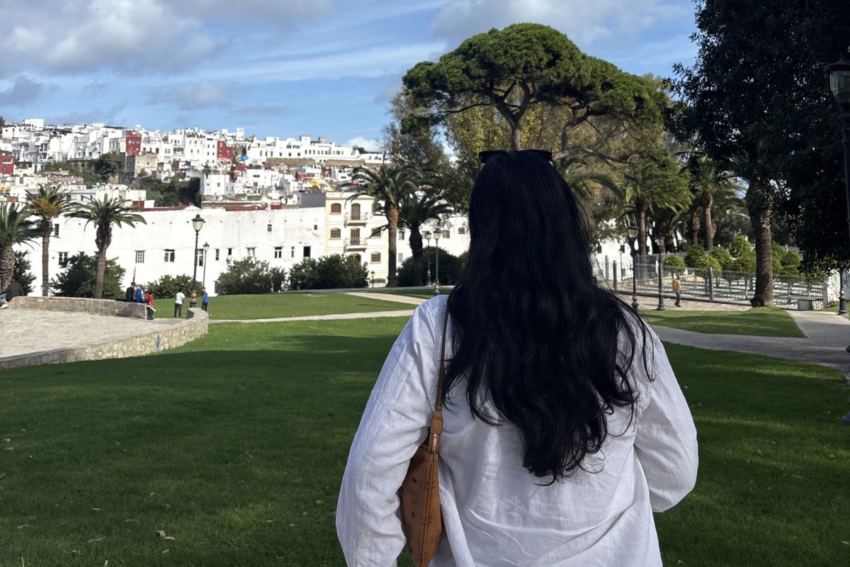 A woman with her back to the camera looking at a city in the background on a sunny day.