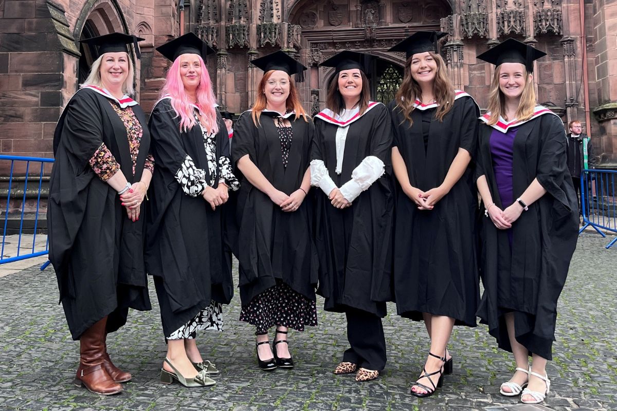 A group of women smiling at the camera, all wearing graduation gowns and caps.