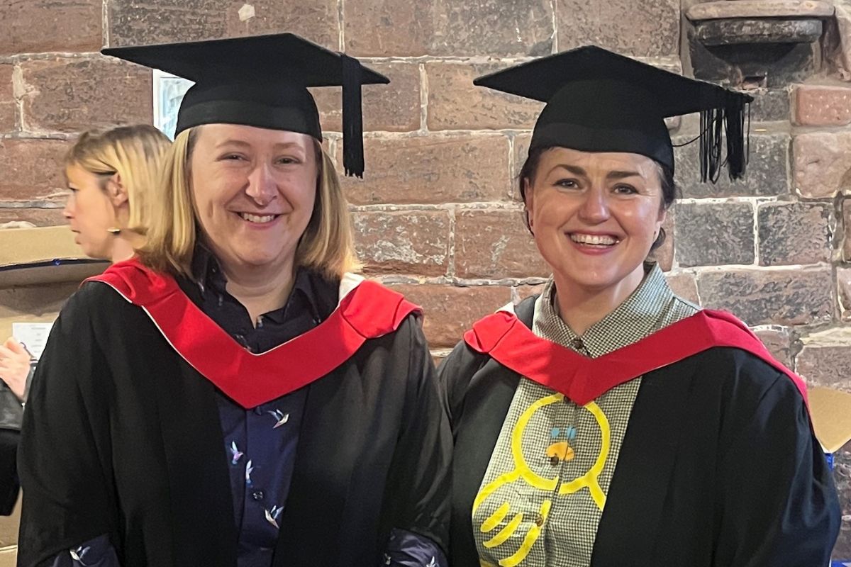 Two women facing the camera, smiling, in graduation gowns and caps.