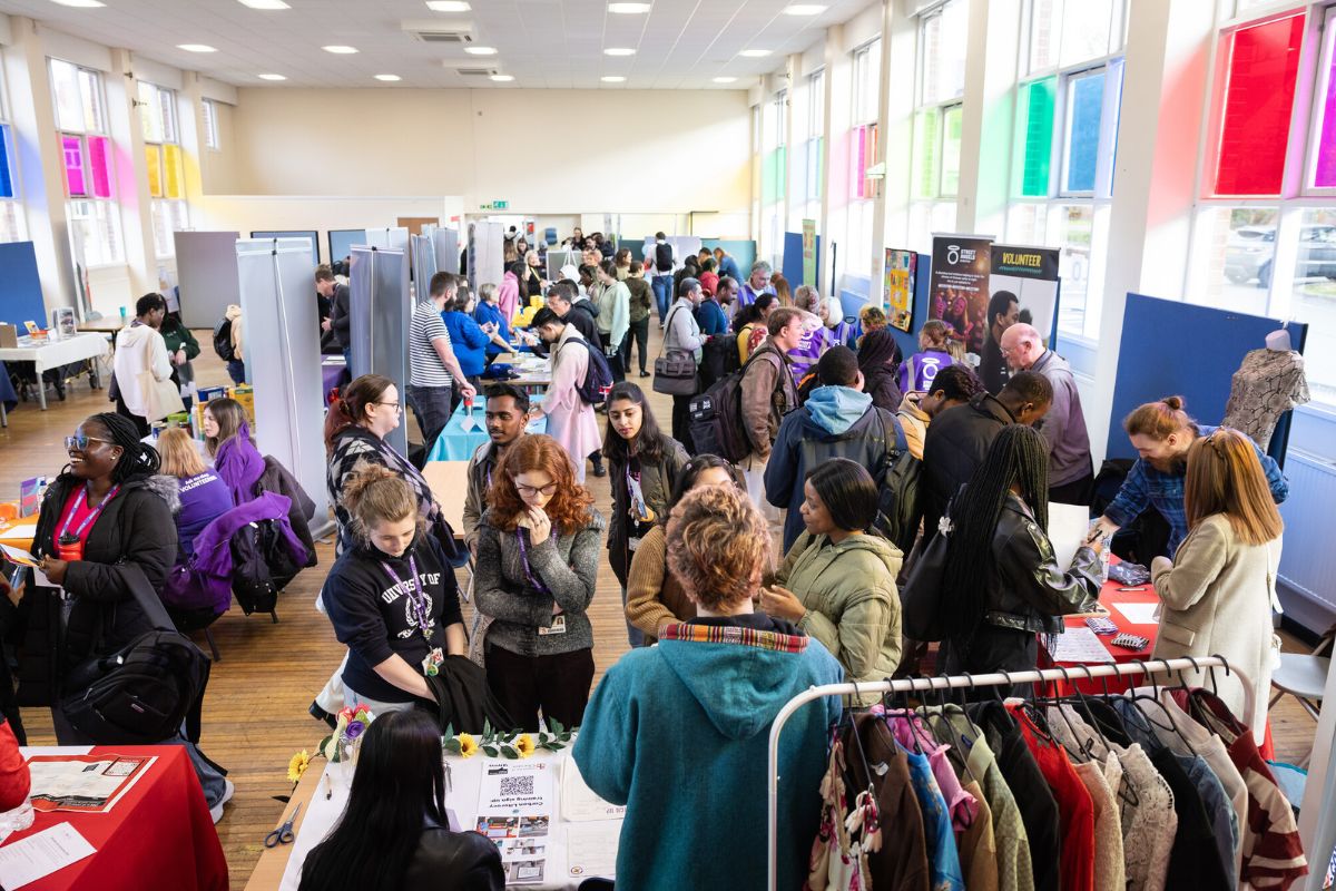 A room filled with manned information stalls and dozens of people walking around.