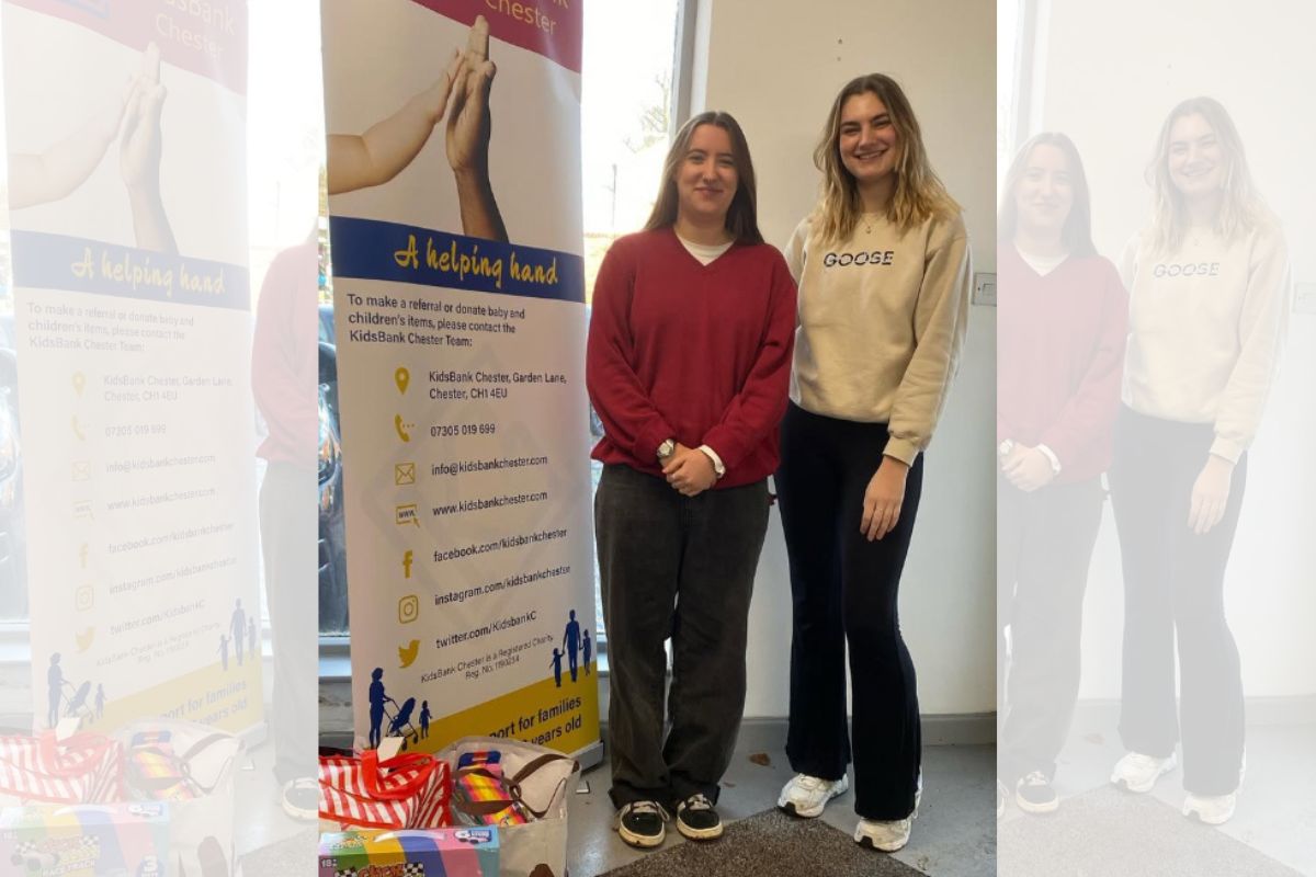 Two female students standing next to a Kidsbank banner and donated toys.
