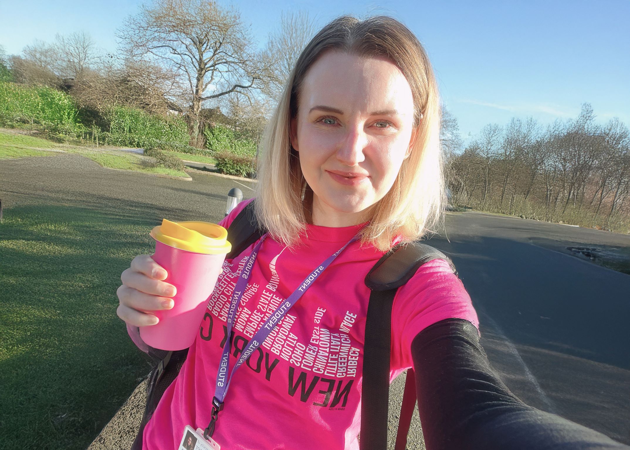 Student standing in car park holding a drink with trees in the background