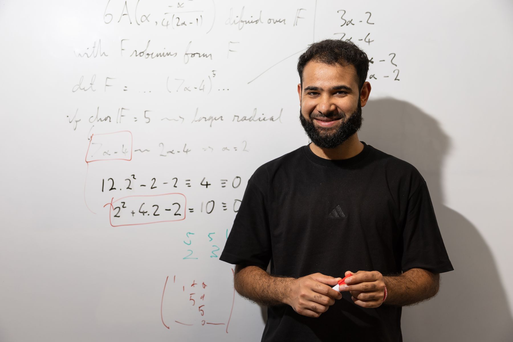 Abdul Wajid Mir standing in front of a whiteboard with complex algebra workings.