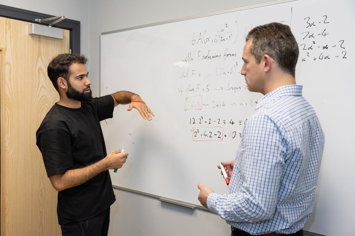Abdul Wajid Mir with Dr Justin McInroy, Senior Lecturer in Mathematics at the University of Chester, discussing algebra in front of a whiteboard.