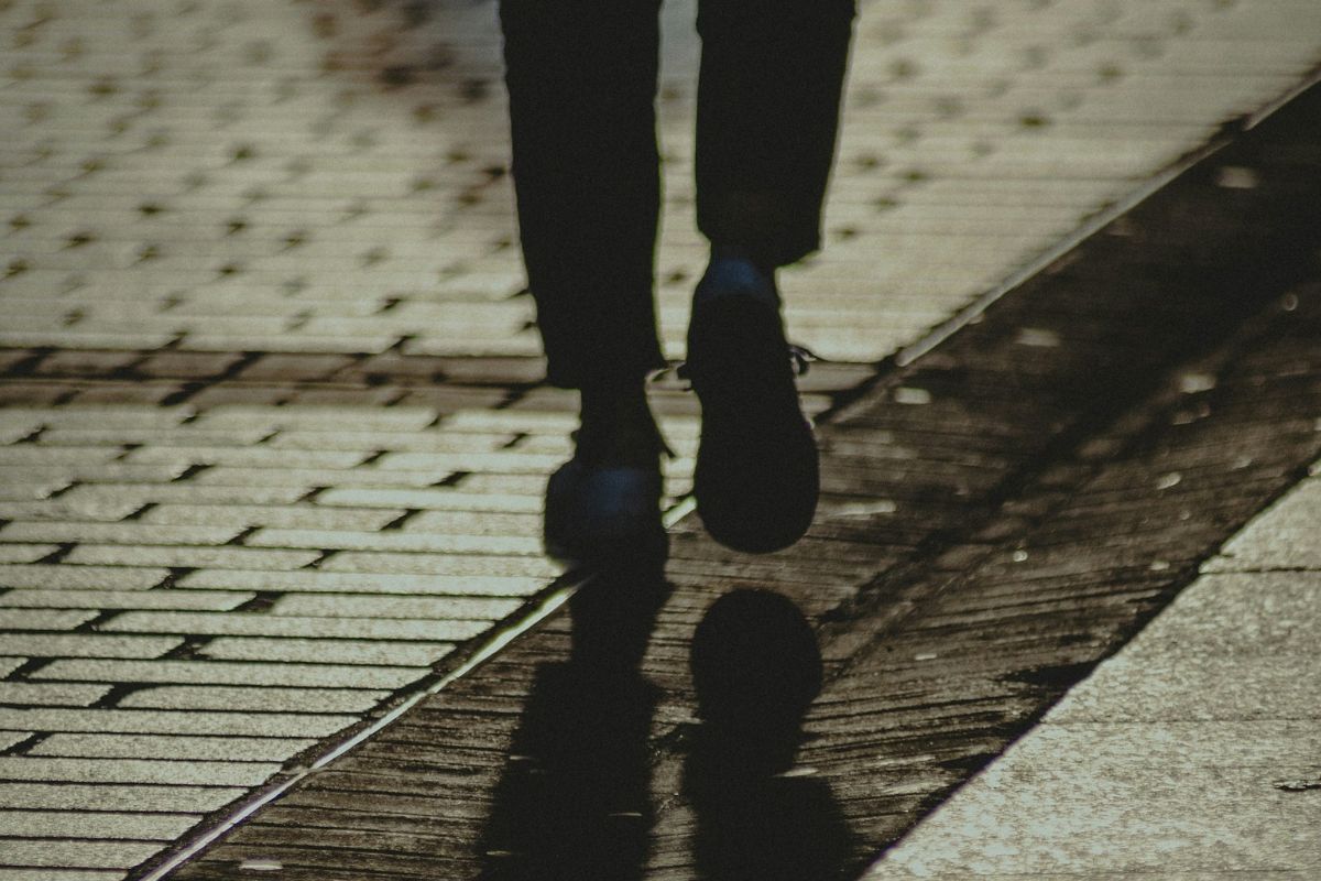A person walking down a street, casting a shadow.