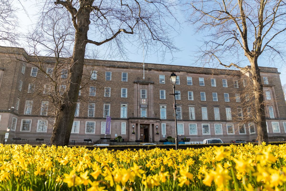 A low-angled landscape image of the Wheeler building, taken from behind a tree and with a floral display in front.