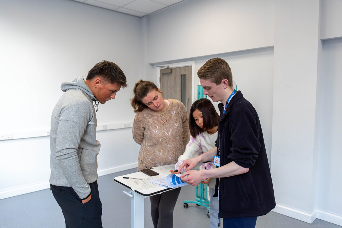 lecturer pointing at book and instructing a group of students