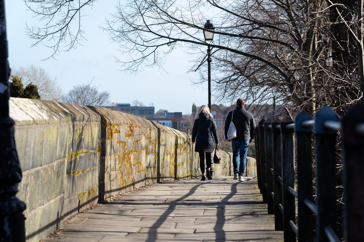 A man walking outdoors on the Chester city roman walls, with a lamp post nearby.