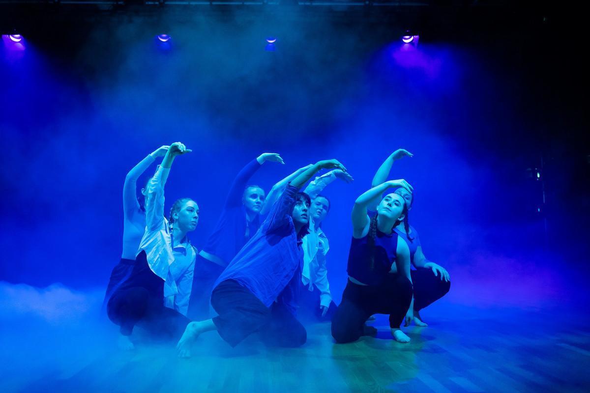 Group of performing arts students in expressive contemporary dance pose on stage under dramatic blue lighting and fog, showcasing creativity and movement for a Performing Arts BA course..