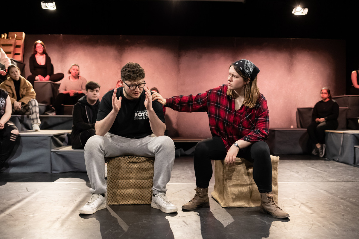 two students sitting on box props on stage during a rehersal performance