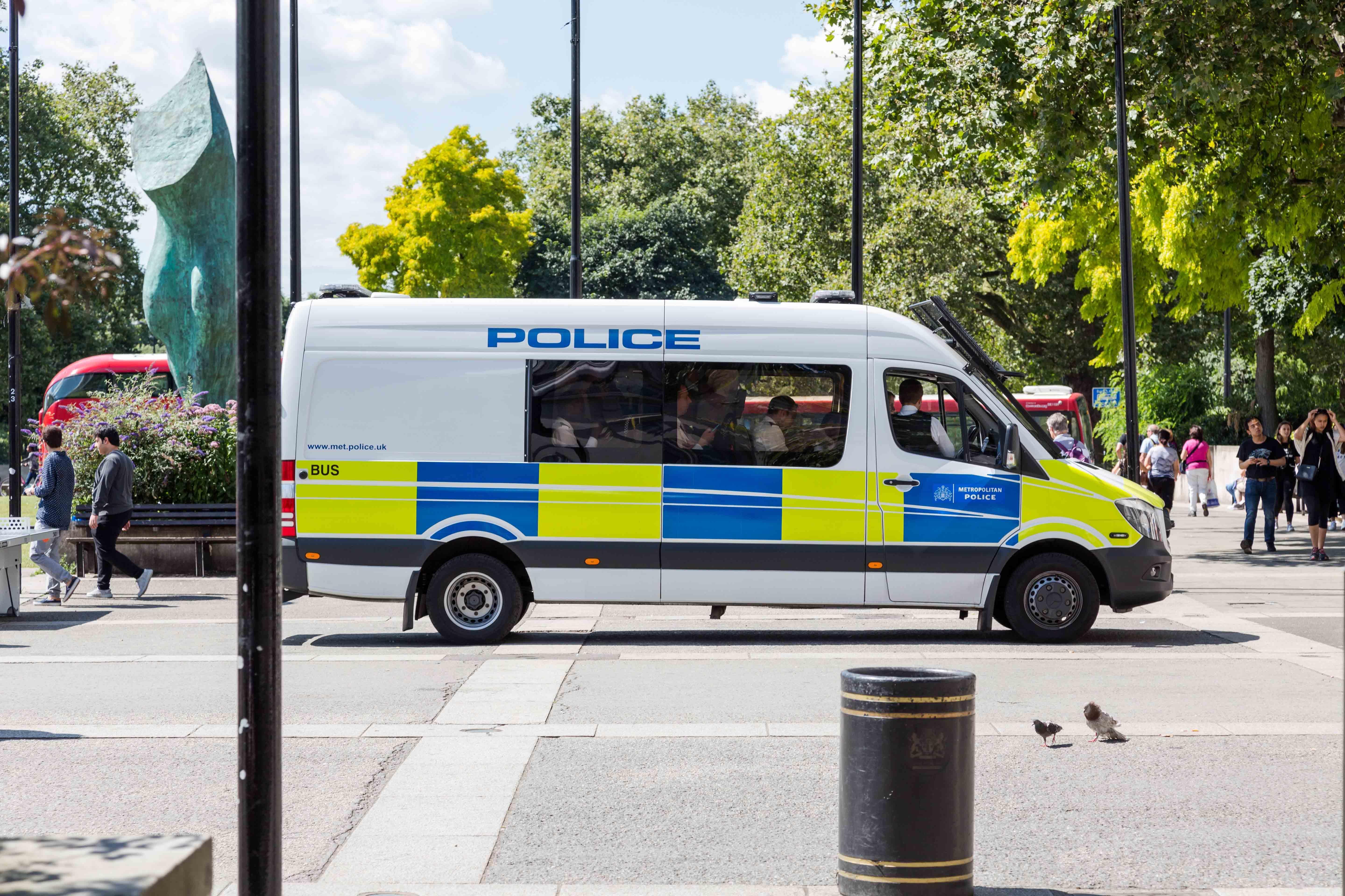 Metropolitan Police van in a busy urban area with pedestrians and greenery, illustrating real-world policing practice and community presence for the Policing, Law and Investigation BSc (Hons) course.
