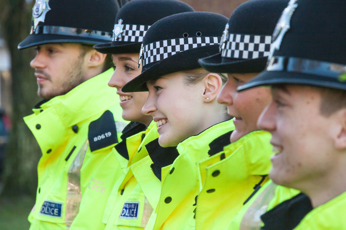 A group of male and female policing students, wearing police uniform standing in a row smiling.