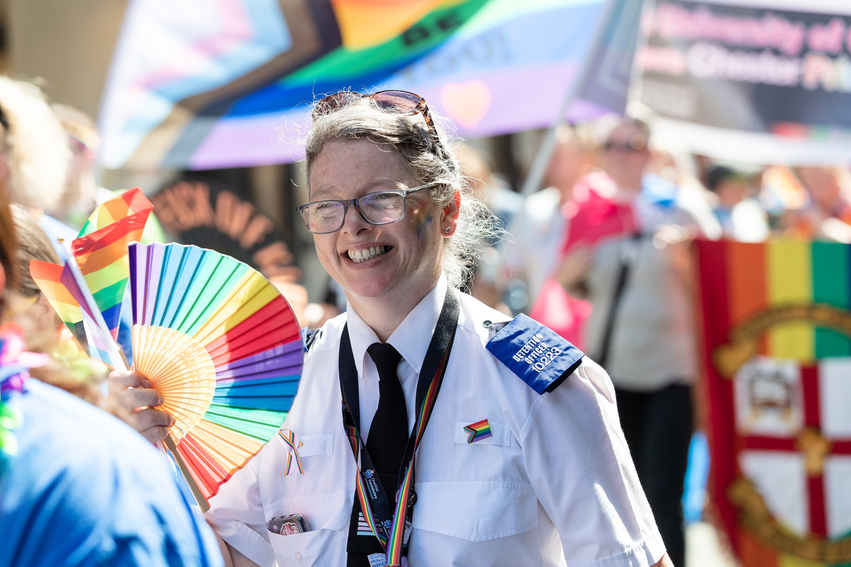 Police woman walking alongside crowds in street during pride parade.