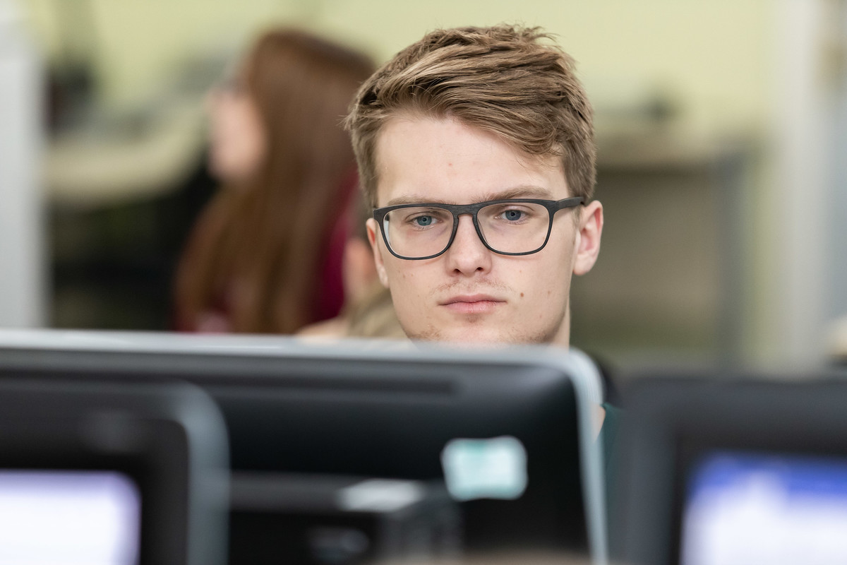 A student looking forward at a desktop computer screen, while others are studying in the background.