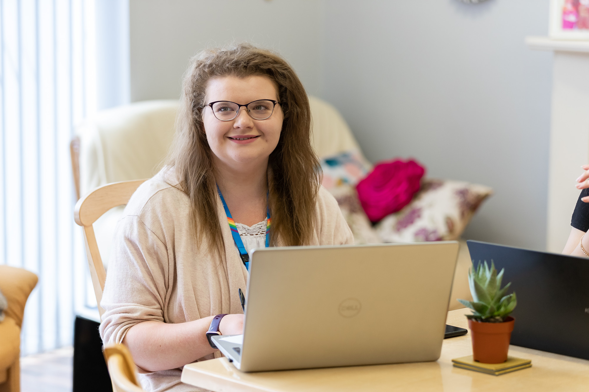 Student, smiling and looking up from laptop while sitting at a table