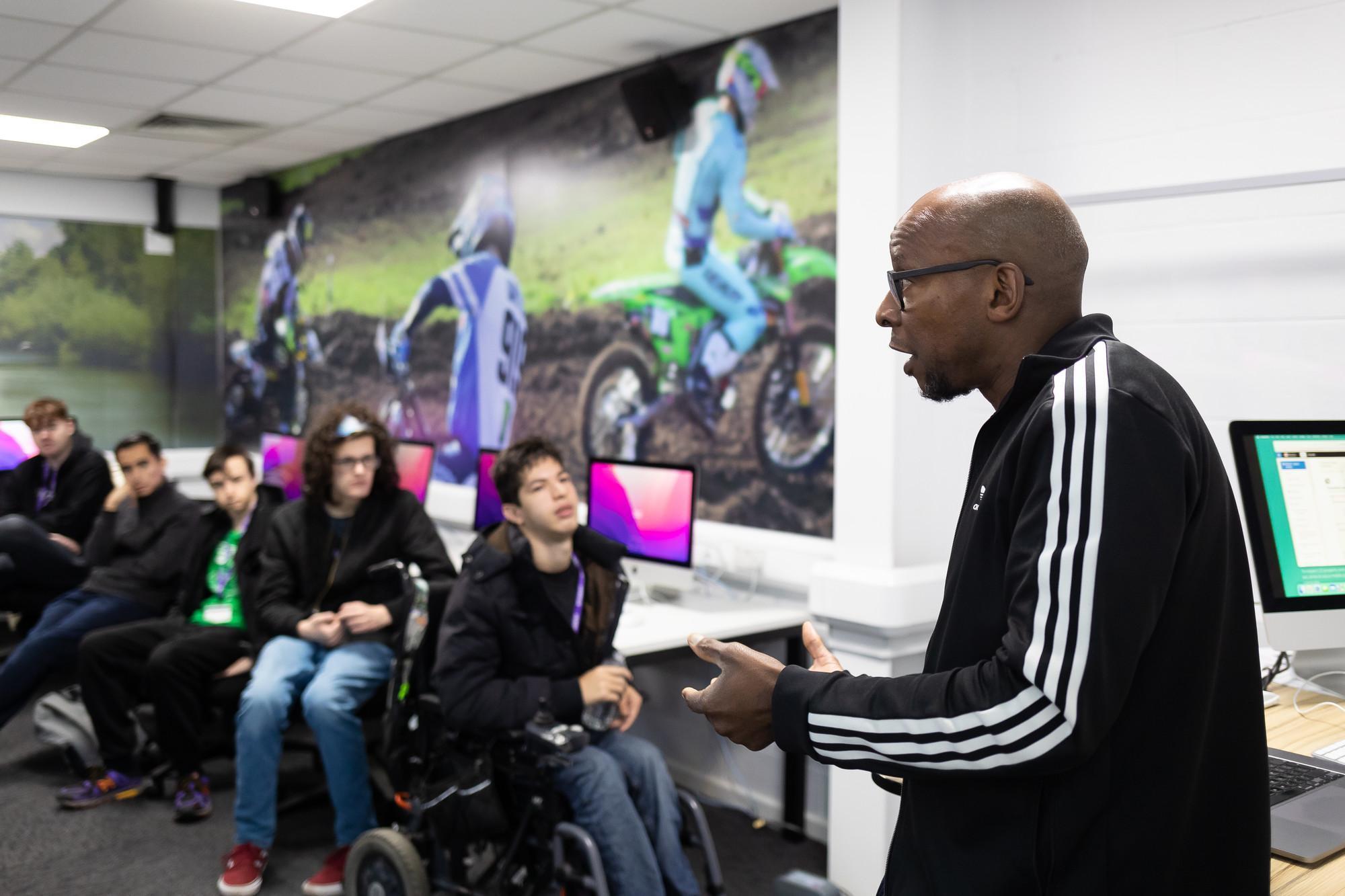 Sports Journalism BA (Hons) class at the University of Chester, showing a lecturer presenting to students in a modern computer lab with sports-themed wall graphics.