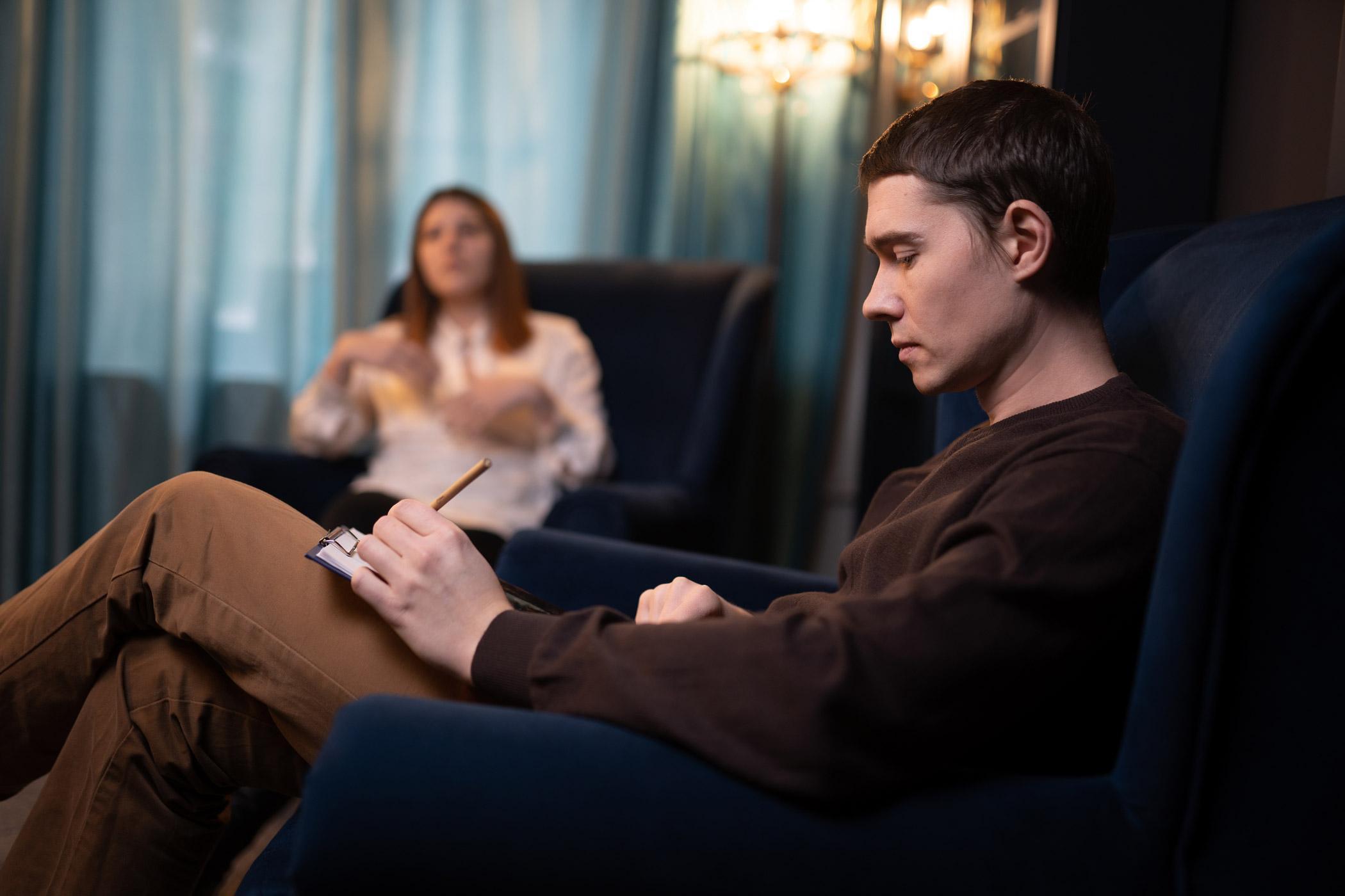 A counsellor takes notes while listening to a person speaking during a session, representing the integration of criminology and counselling skills in understanding and supporting individuals within the justice system.