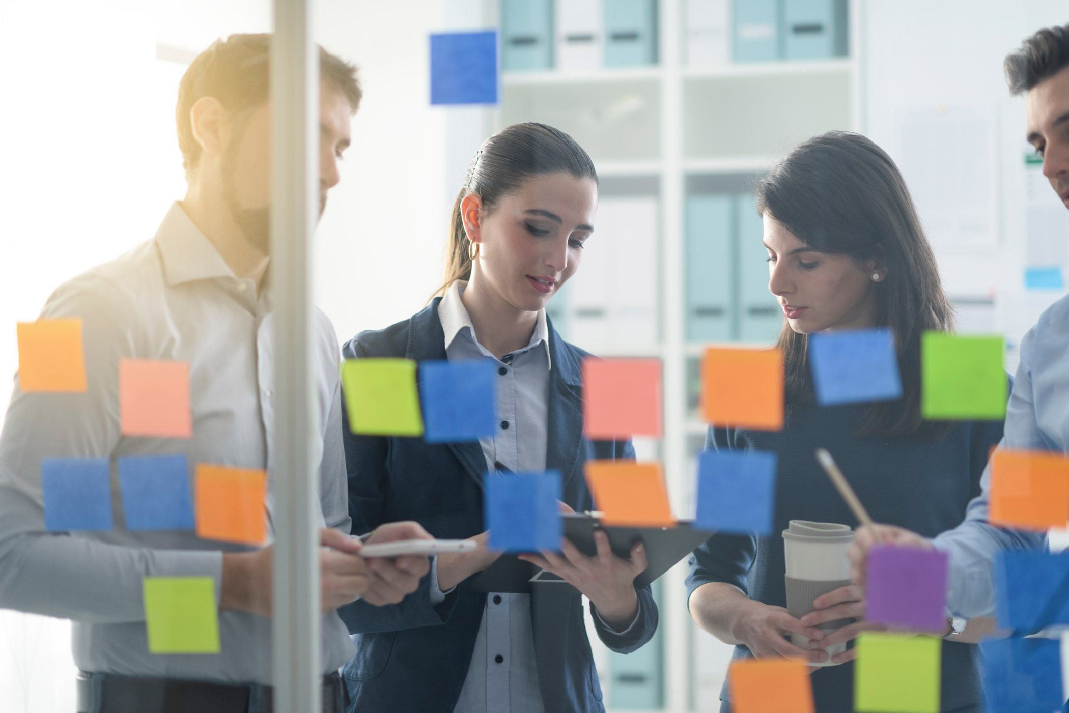 A group of business people stood together looking at notes stuck to a glass window