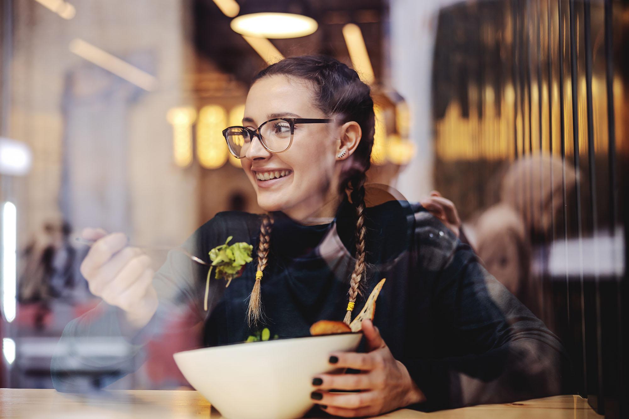 Smiling student eating a healthy meal in a café, representing the Nutrition BSc (Hons) degree at the University of Chester focused on food, health, and wellbeing.
