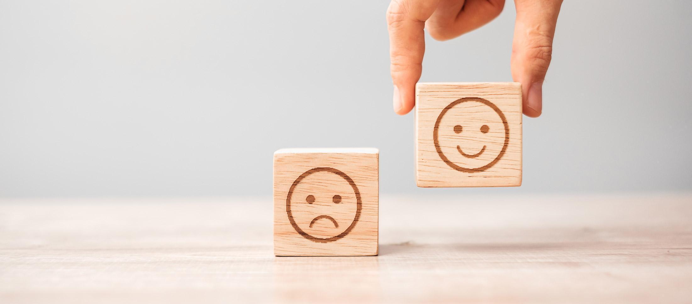 Close-up of wooden emotion blocks showing sad and happy faces, symbolising psychological wellbeing, behaviour change and mental health studies for Psychology (Conversion) MSc students at the University of Chester.