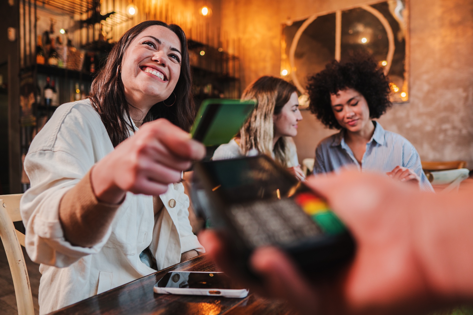 Happy young woman paying bill with a contactless credit card in a restaurant.