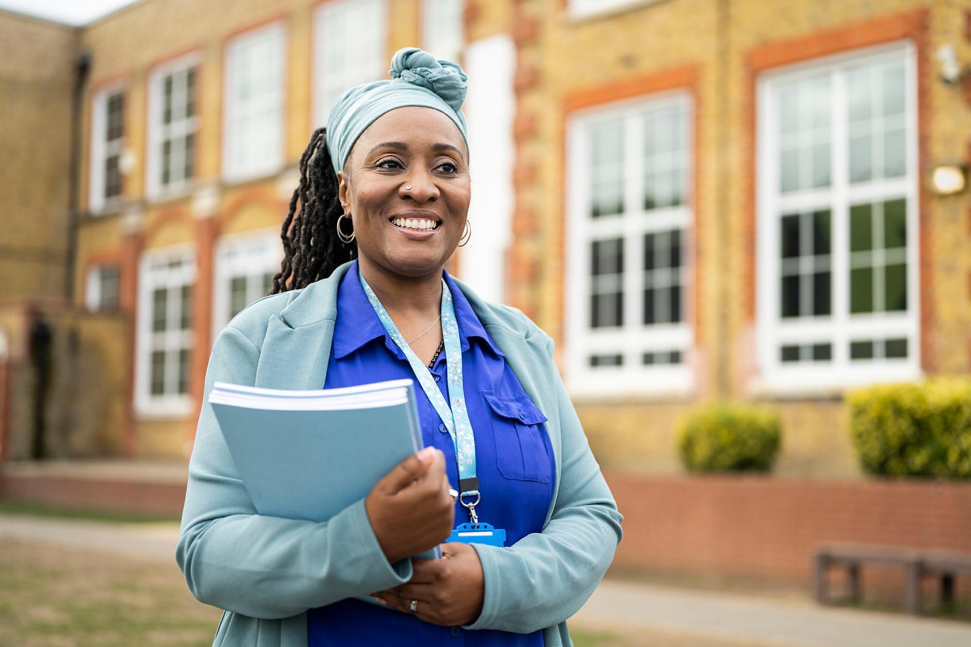 Doctor of Education (EdD) student standing outside a university building, holding study materials. Advance educational leadership, professional practice and research expertise with the University of Chester's Doctor of Education EdD programme.