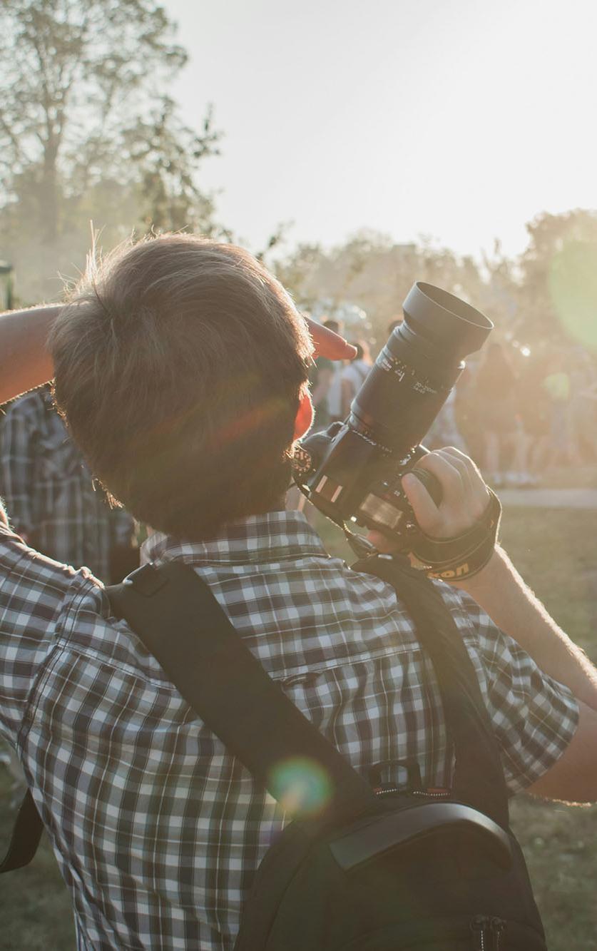 Man in grey and white plaid shirt with backpack and DSLR camera on hand