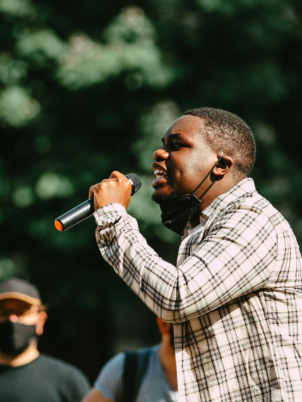 Man in blue and white plaid dress shirt holding microphone