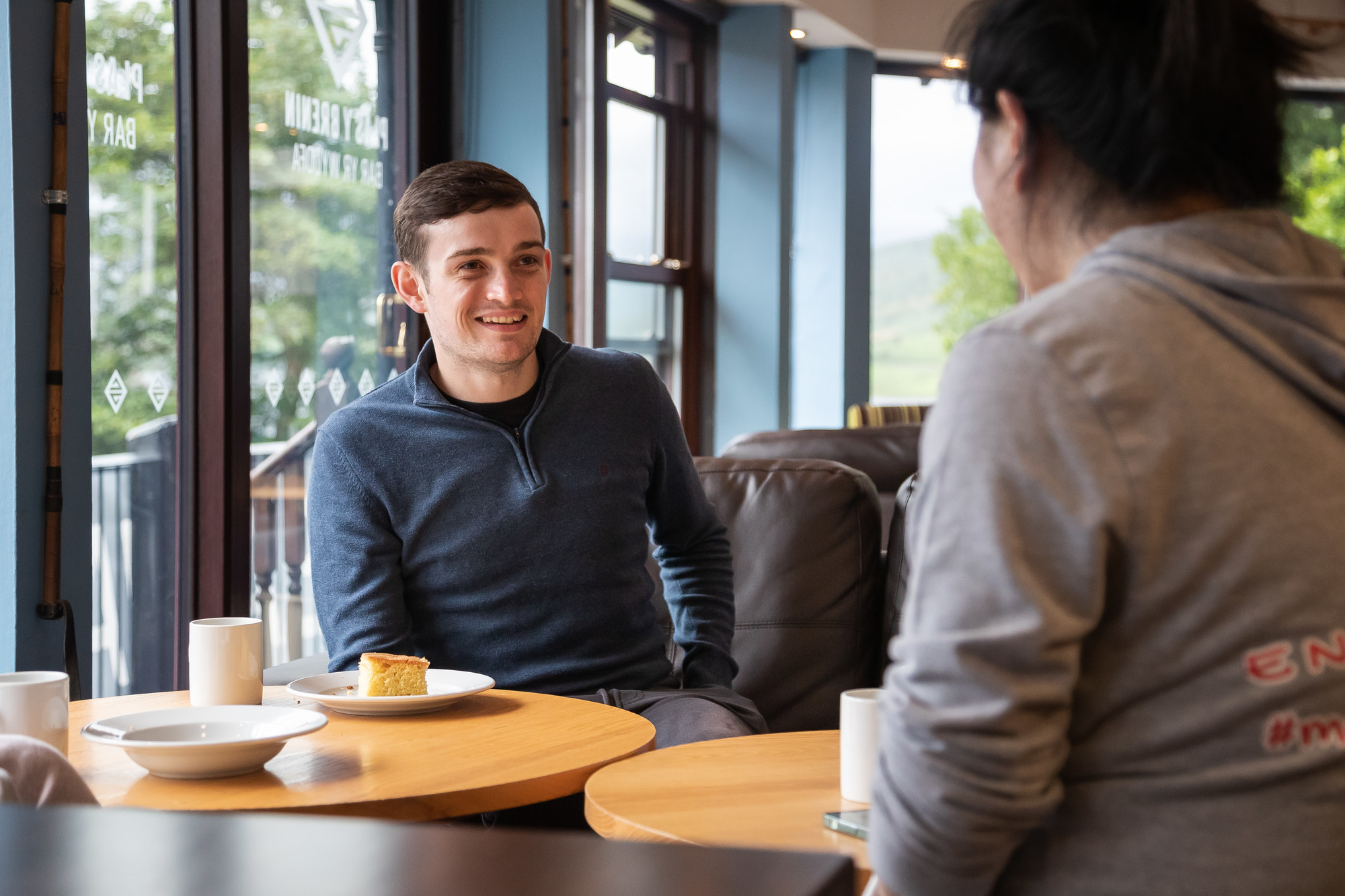 Two students chatting over coffee and cake in a bright, welcoming campus café.