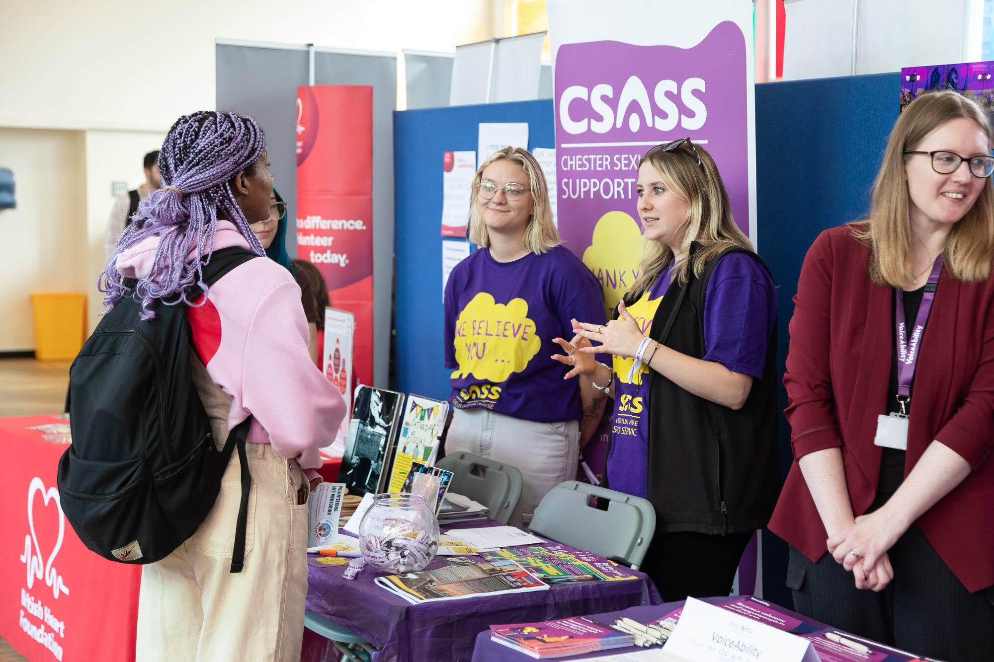 Students speak with volunteers at a Chester Sexual Assault Support Service (CSASS) information stall during a university volunteering or wellbeing fair.