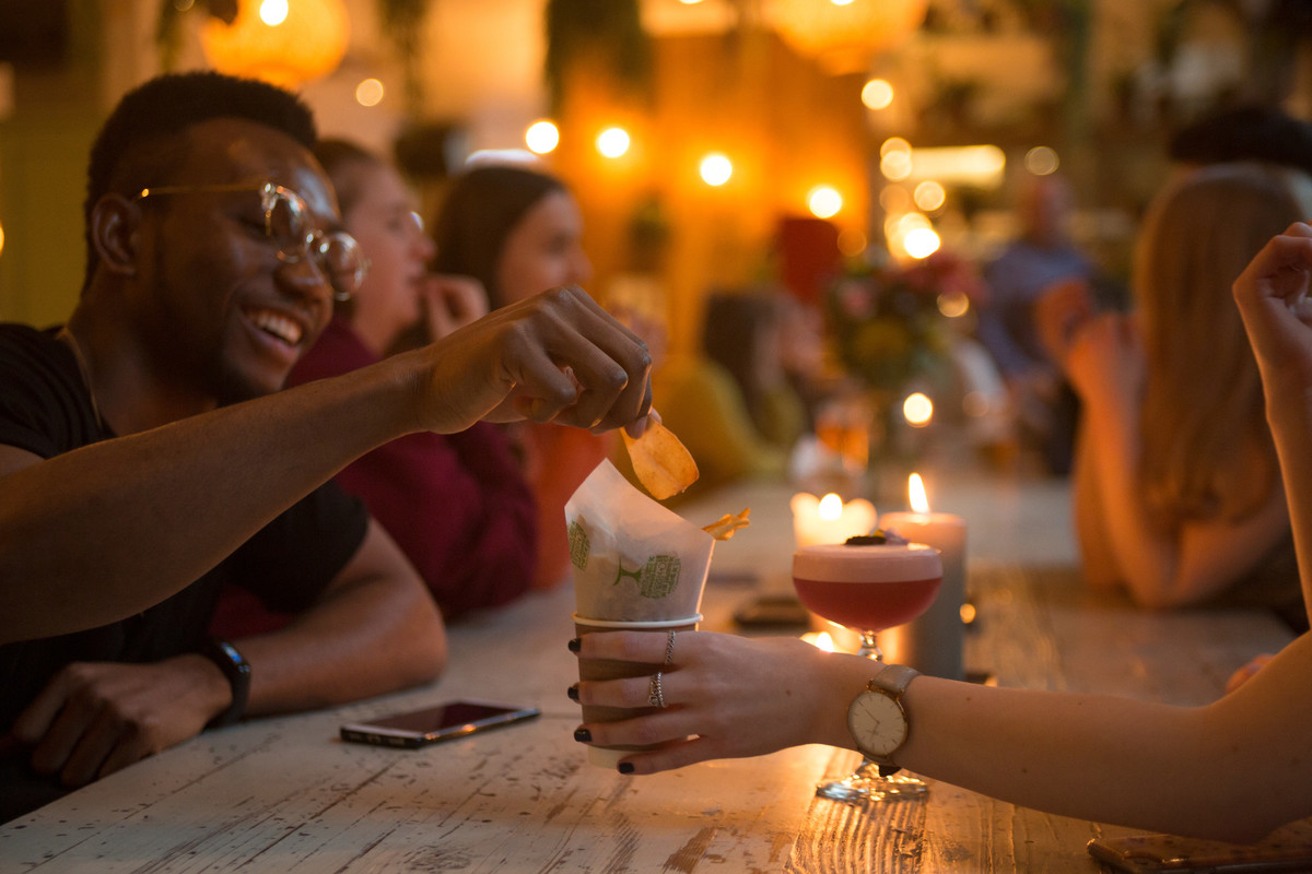 Students at a bar, sitting at a large, long table, sharing food and drinks
