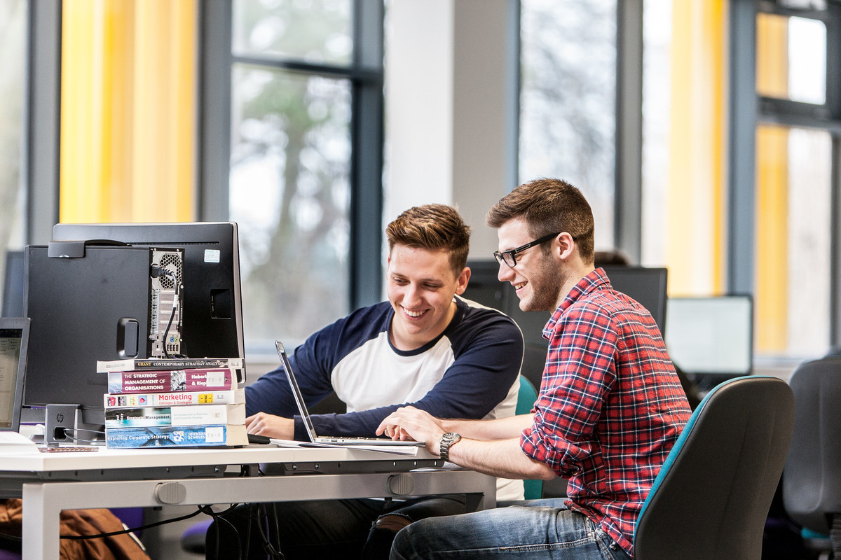 Two students sat at a computer workstation with books