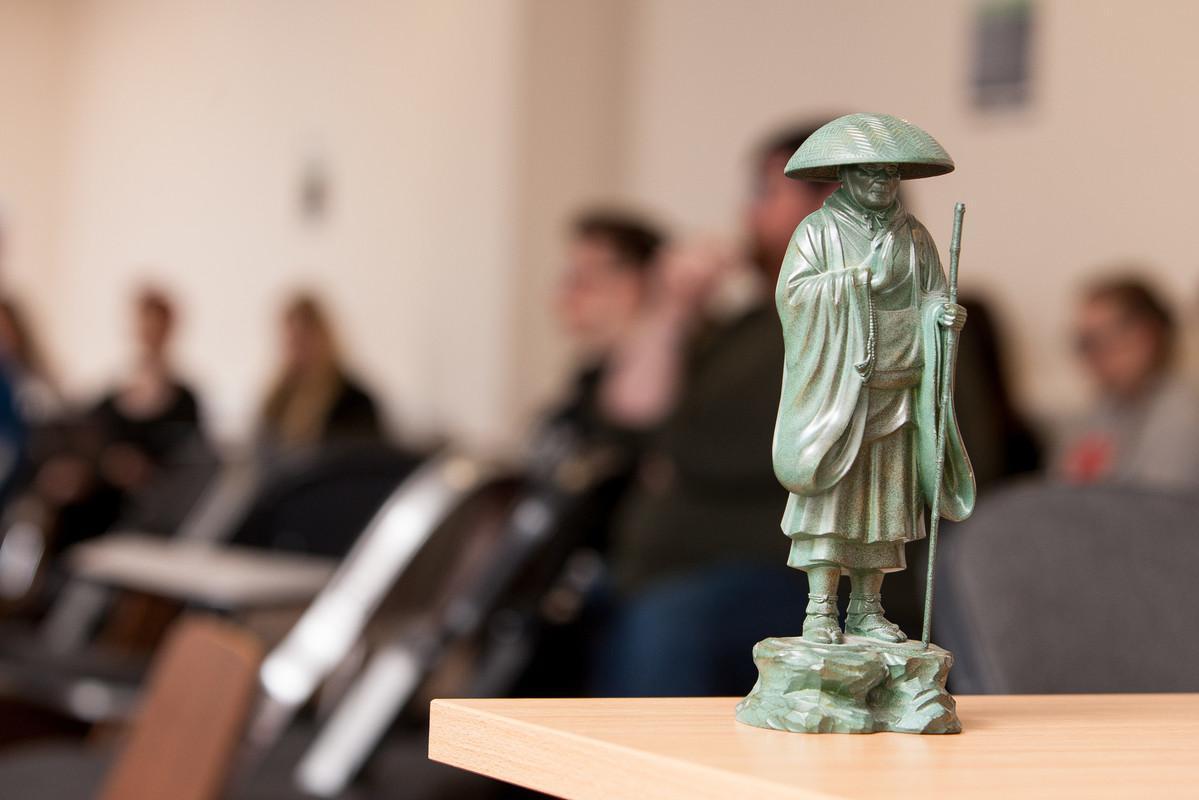 Philosophy, Ethics and Religion BA (Hons) students attending a university seminar with a statue of a Buddhist monk symbolizing spirituality, reflection and ethical study.