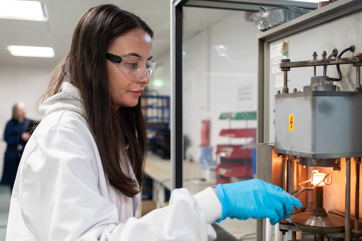 A female student, wearing white coat and protective glasses, and blue gloves while working in a laboratory