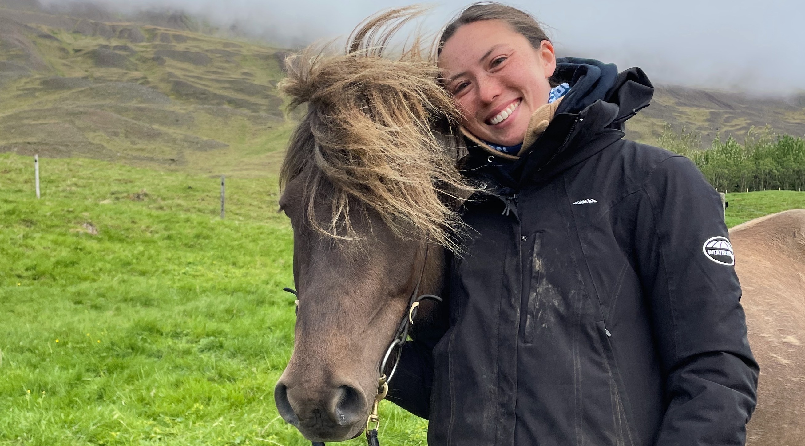 A student standing alongside a horse in a field